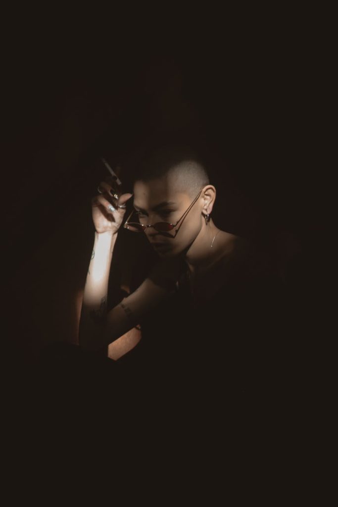 light and shadow photo of woman in dark room holding a cigarette