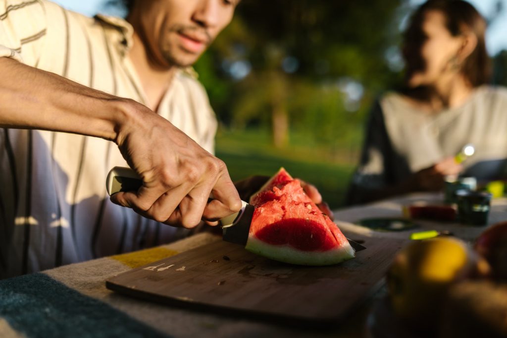 man slicing watermelon on brown wooden chopping board